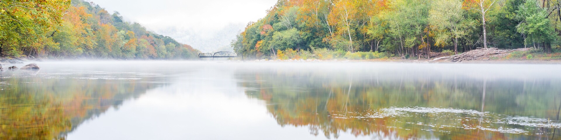 New River Gorge wide canyon water river lake during autumn golden orange foliage in fall by Grandview with peaceful calm tranquil morning bright mist fog