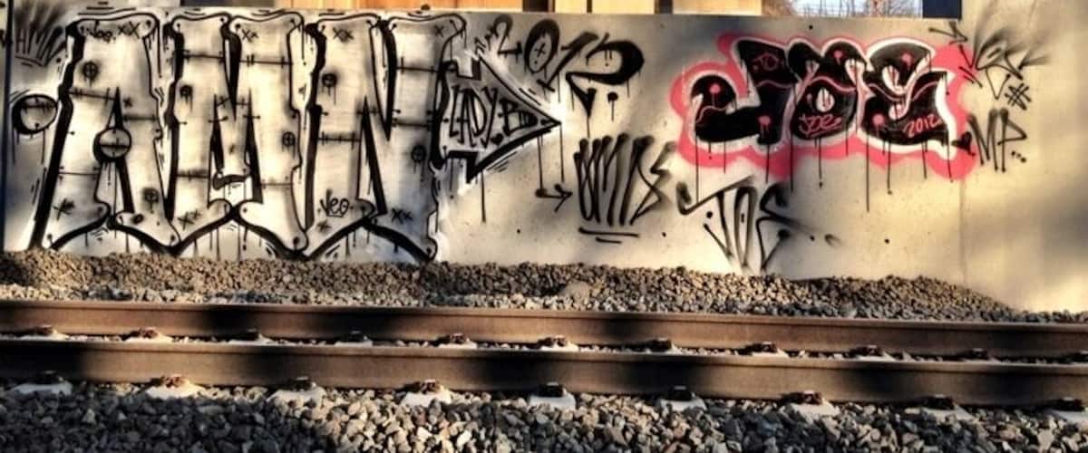 A railway track under a concrete bridge with graffiti on the wall.
