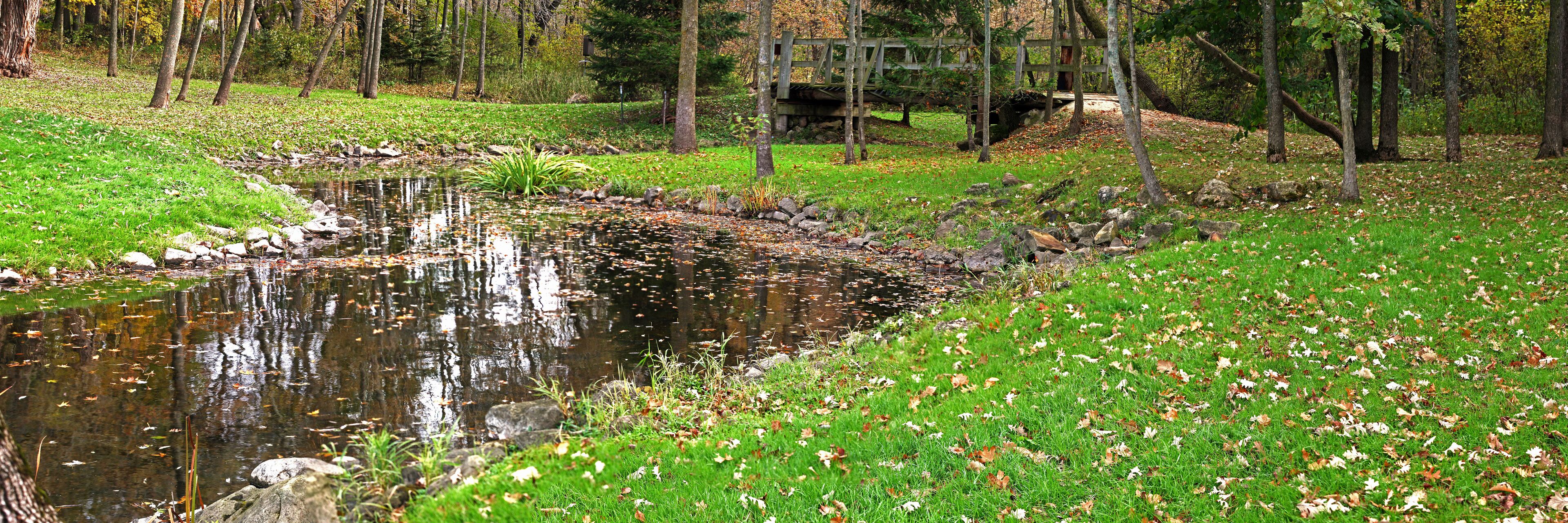 Rural County Park  Wisconsin, stream winding through a woods and prairie, with a small foot bridge in the background. Panorama 