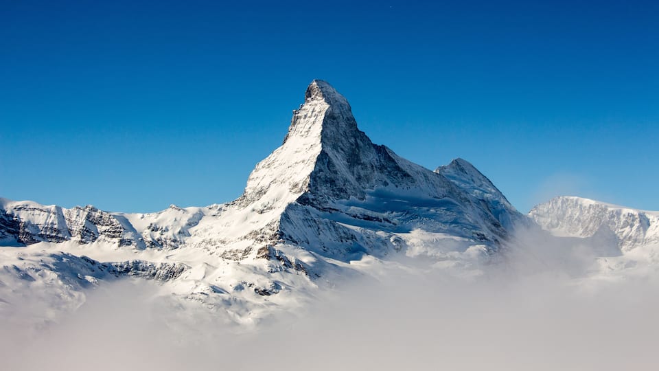 A snow-covered mountain peak with sharp ridges and a clear blue sky.