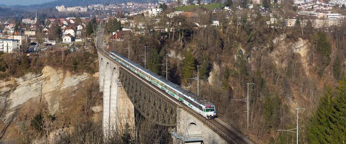 A train crossing a bridge over a valley with a town in the background.