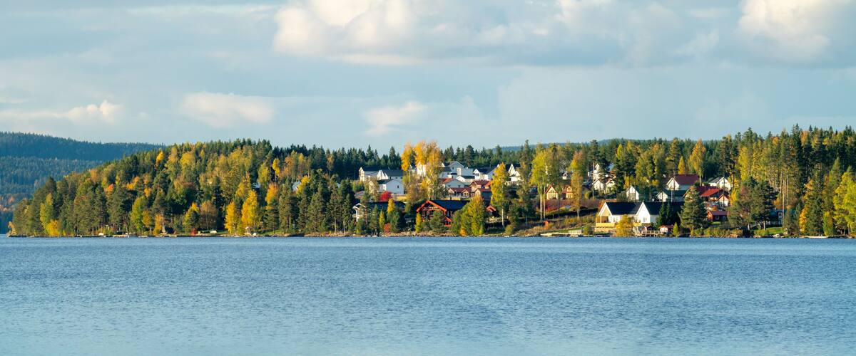 A lakeside village with houses and trees, surrounded by hills.