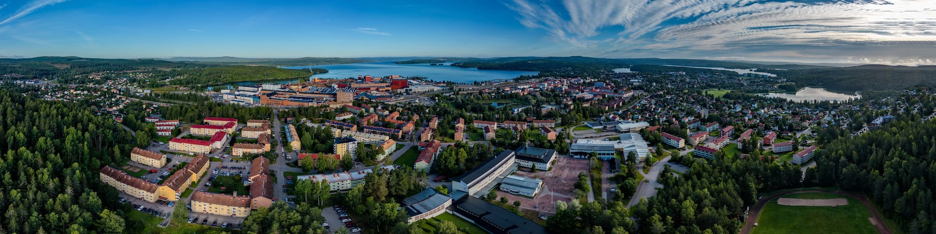 An aerial view of a town with a lake, surrounded by dense forests and featuring a prominent red building.