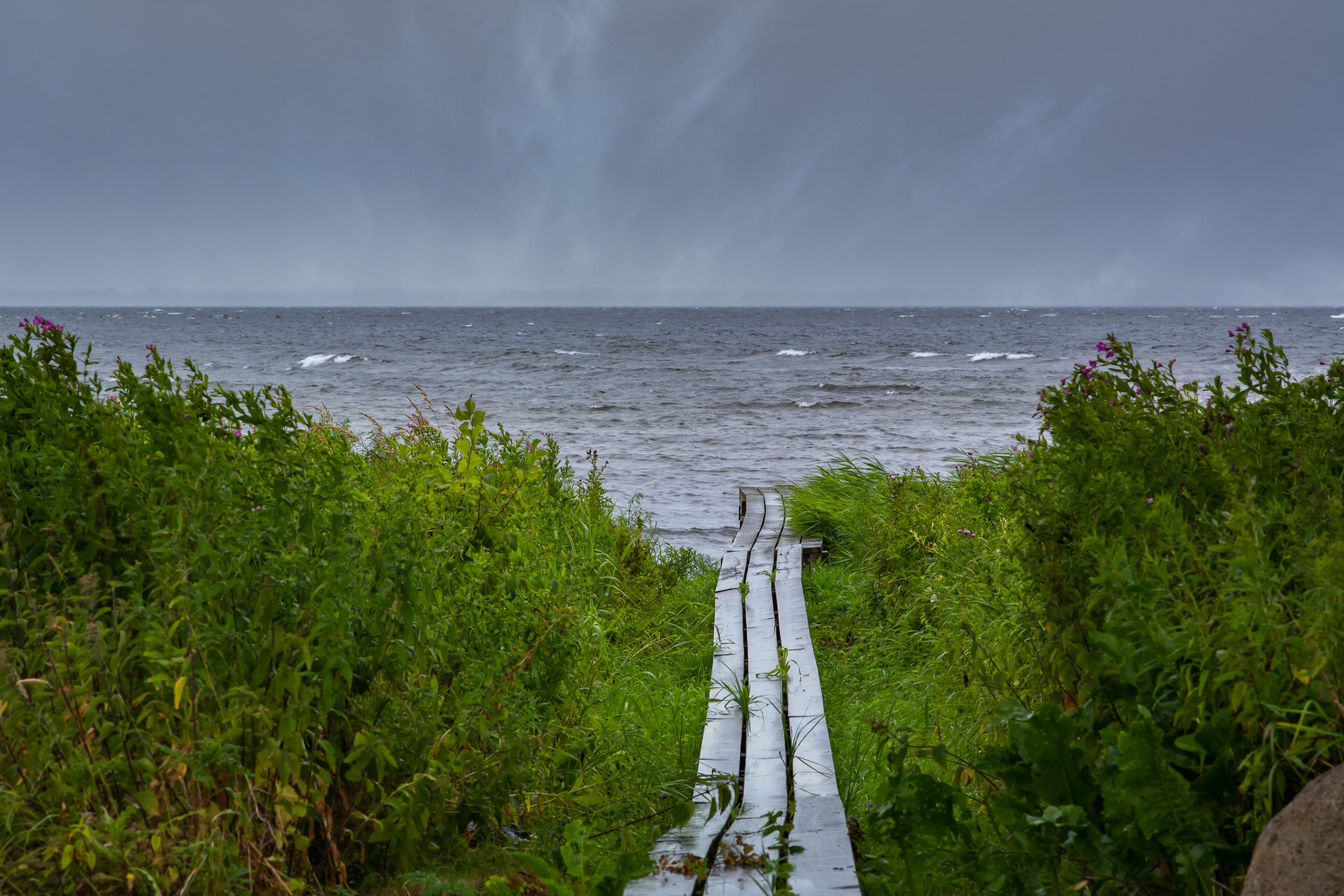 A boardwalk with the blue ocean in the background. Dark dramatic clouds. The picture was taken near Loddekopinge in Scania, southern Sweden