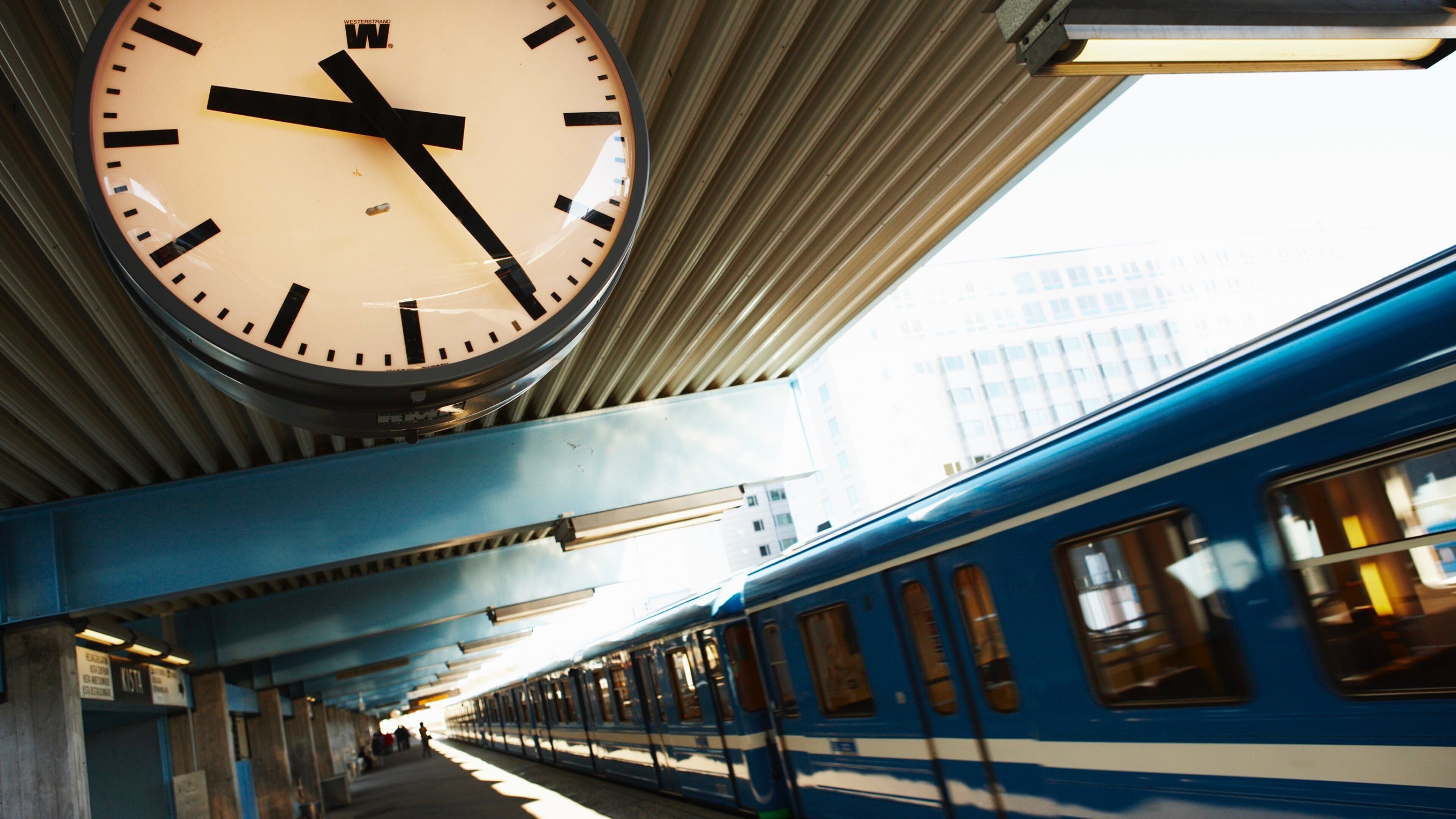 A train station with a clock, platform, and a blue train.