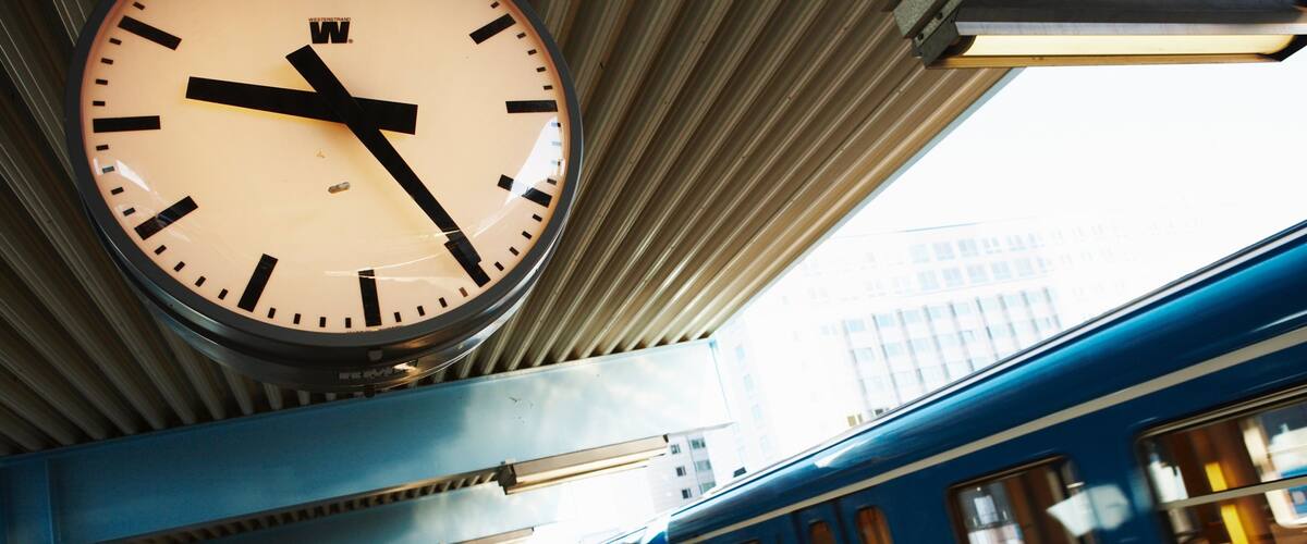 A train station with a clock, platform, and a blue train.