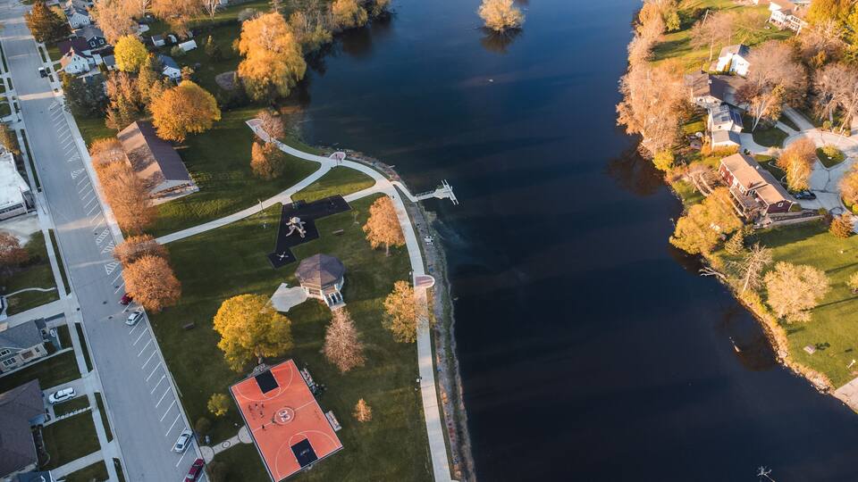 An aerial view of a lakeside community with a basketball court, a gazebo, and residential houses.