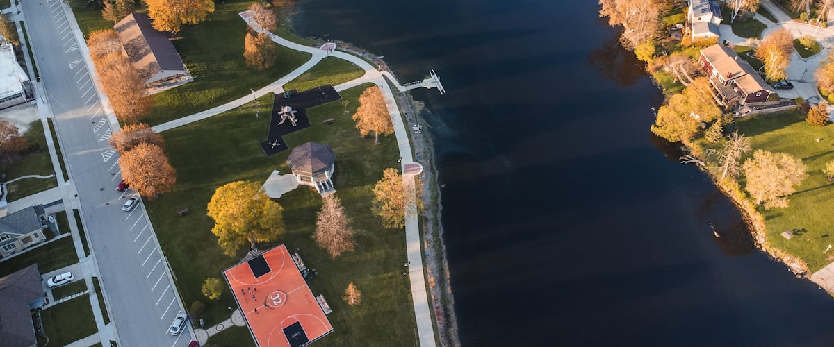 An aerial view of a lakeside community with a basketball court, a gazebo, and residential houses.