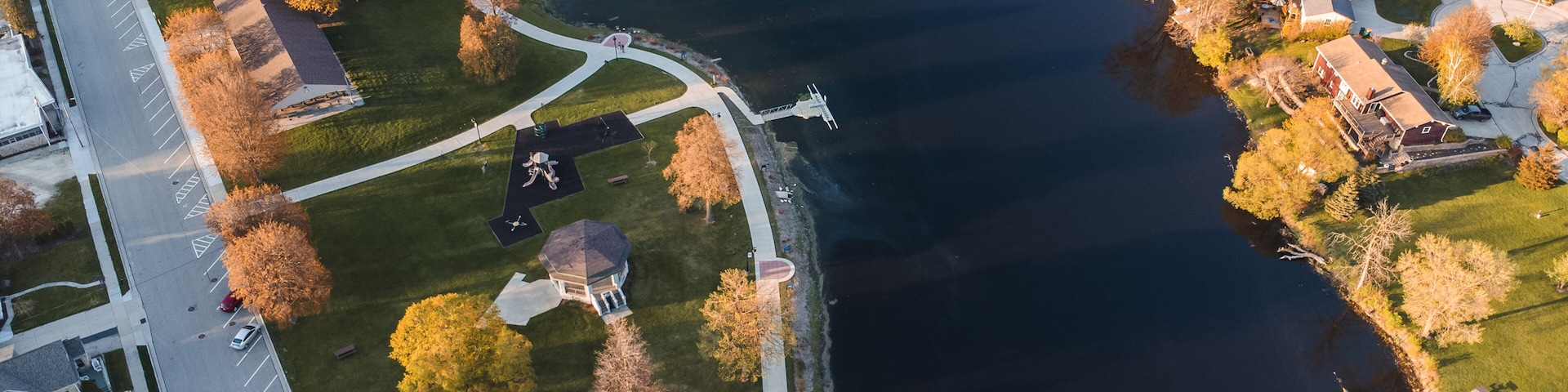 An aerial view of a lakeside community with a basketball court, a gazebo, and residential houses.