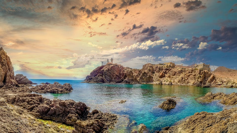 A coastal landscape with rocky formations, clear blue waters, and a dramatic sky.
