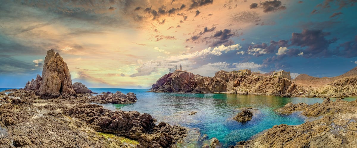 A coastal landscape with rocky formations, clear blue waters, and a dramatic sky.
