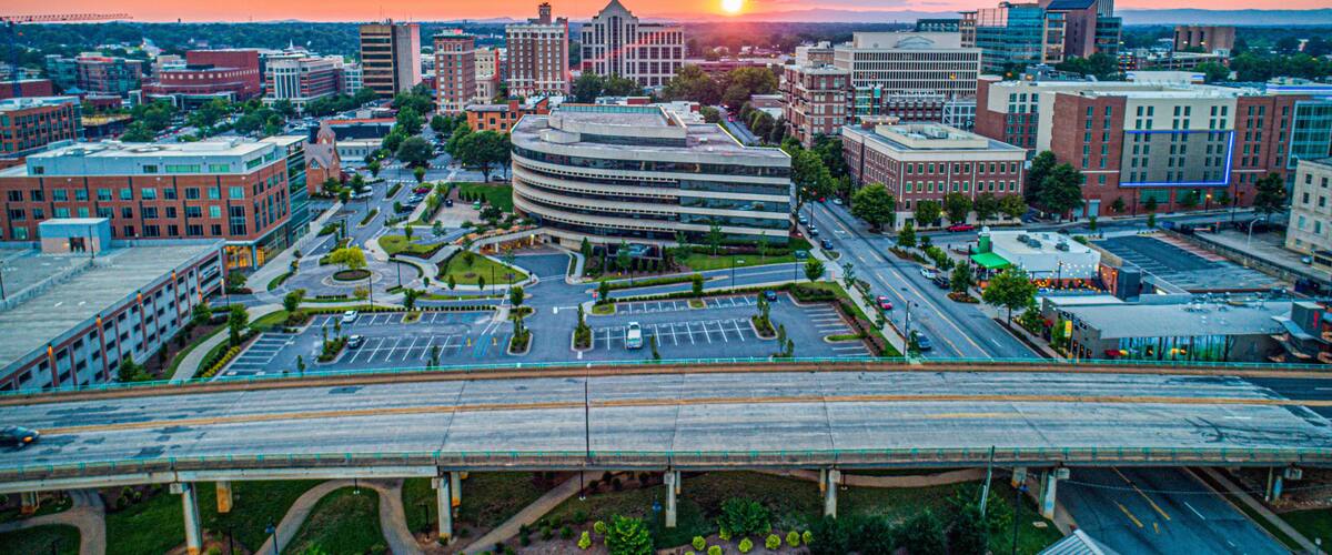A cityscape with a prominent curved building, a bridge, and a sunset.