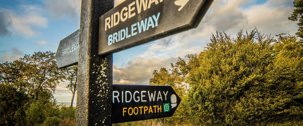 A signpost with directions to Ridgeway and Bridleway, and a footpath symbol.