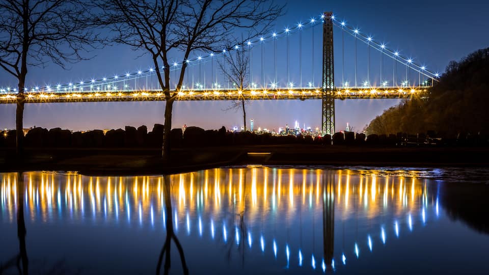 A bridge at night with lights reflecting on water.
