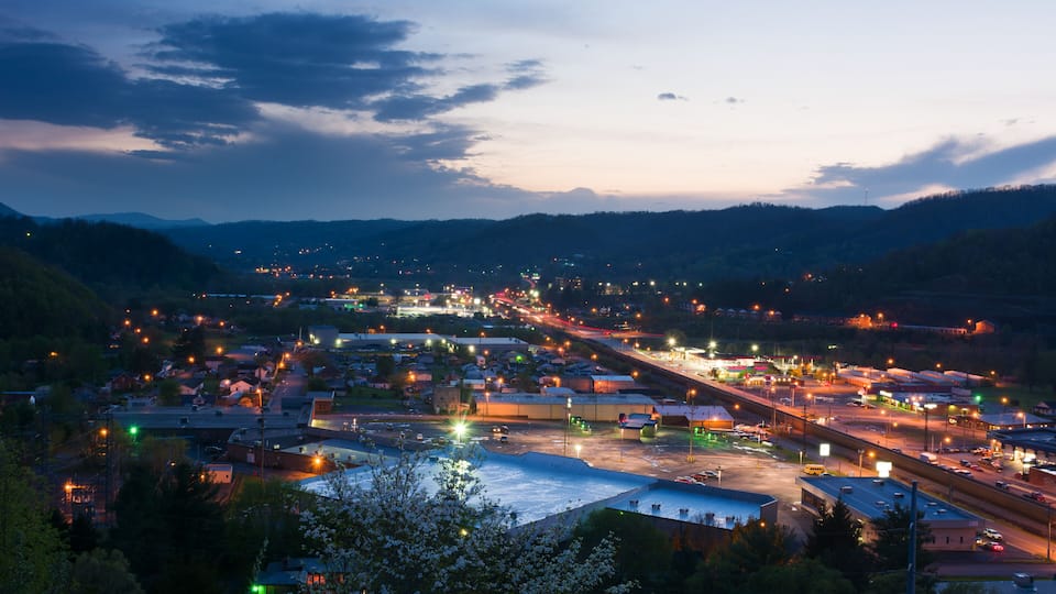 A town at dusk with illuminated streets and buildings, surrounded by hills.