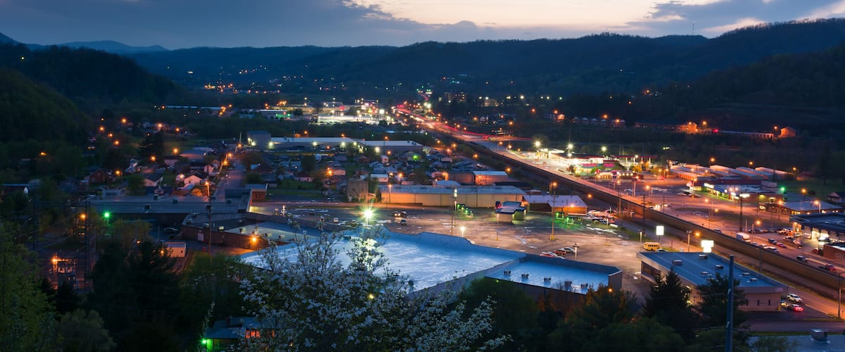 A town at dusk with illuminated streets and buildings, surrounded by hills.