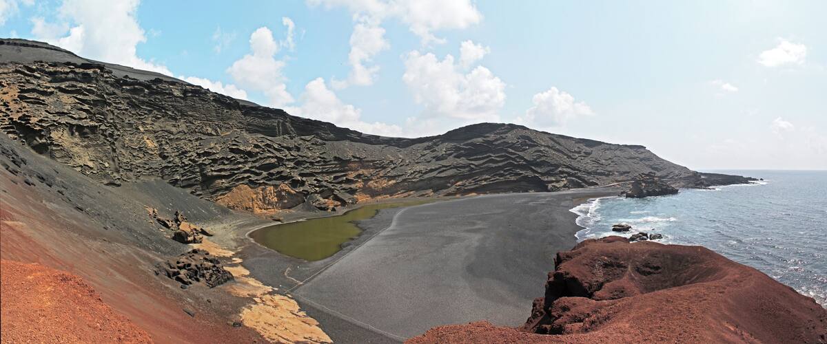 A coastal landscape with a beach, rocky cliffs, and a small green pond.