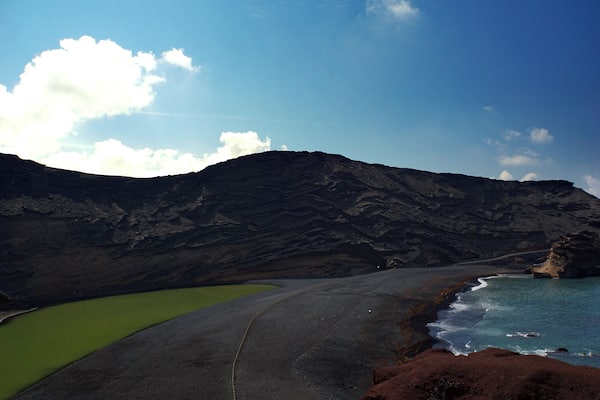 El Lago Verde, formed in an old volcano crater, its natural green colour and the vibrant red rock add dramatic spin to the deep blue of the ocean and the black sand beach - barren volcanic landscape #LifeAtExpedia #SeasideDiscoveriesâ