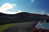 Un paysage côtier avec une plage verdoyante, des falaises rocheuses et un ciel bleu clair.