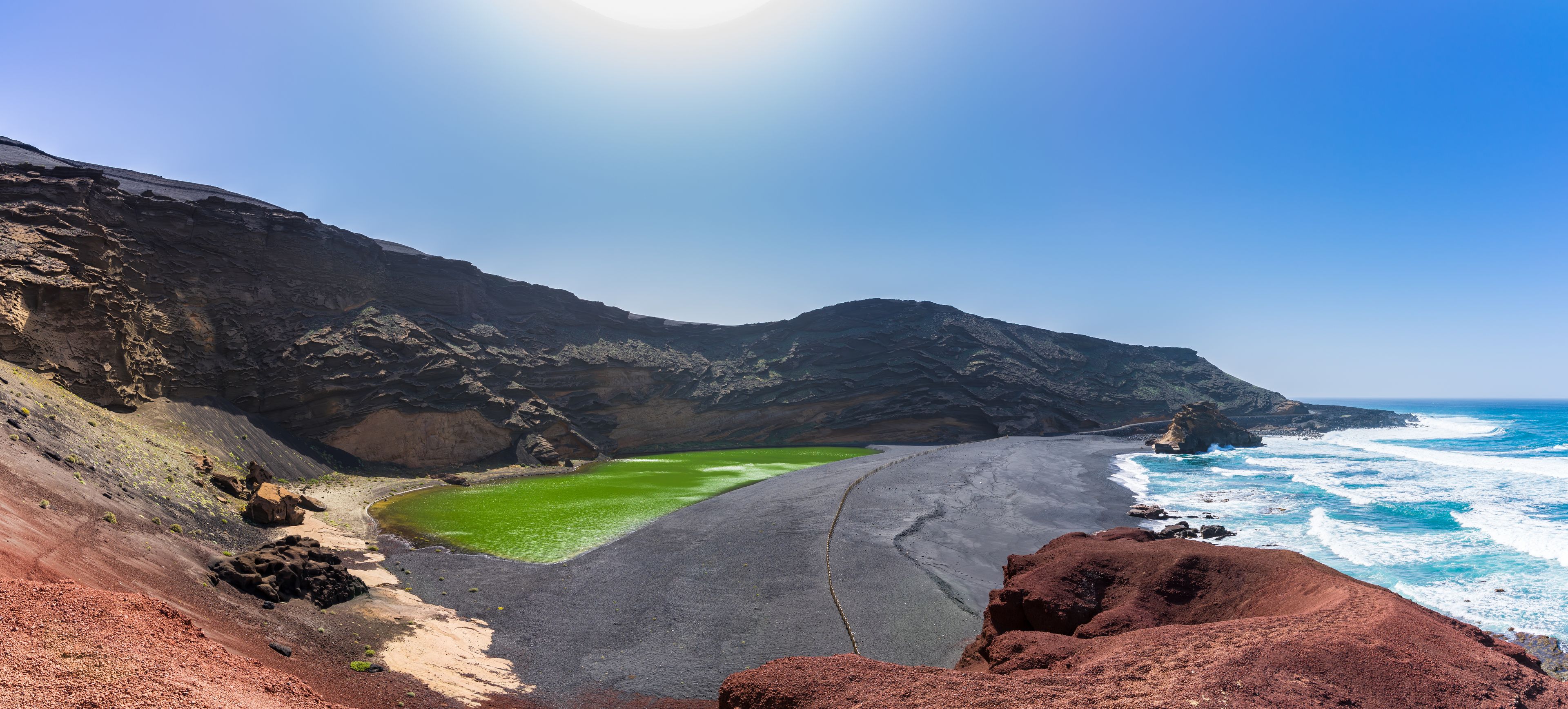 A coastal landscape with a green lagoon, a sandy beach, and rocky cliffs.