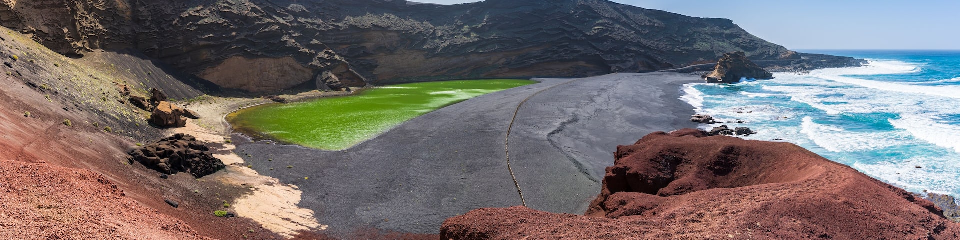 A coastal landscape with a green lagoon, a sandy beach, and rocky cliffs.