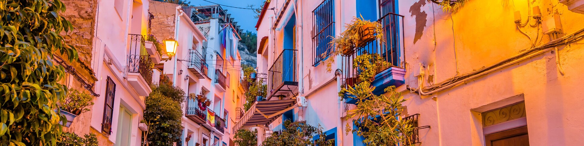 A narrow street with steps leading up to a building, surrounded by colorful buildings and potted plants.