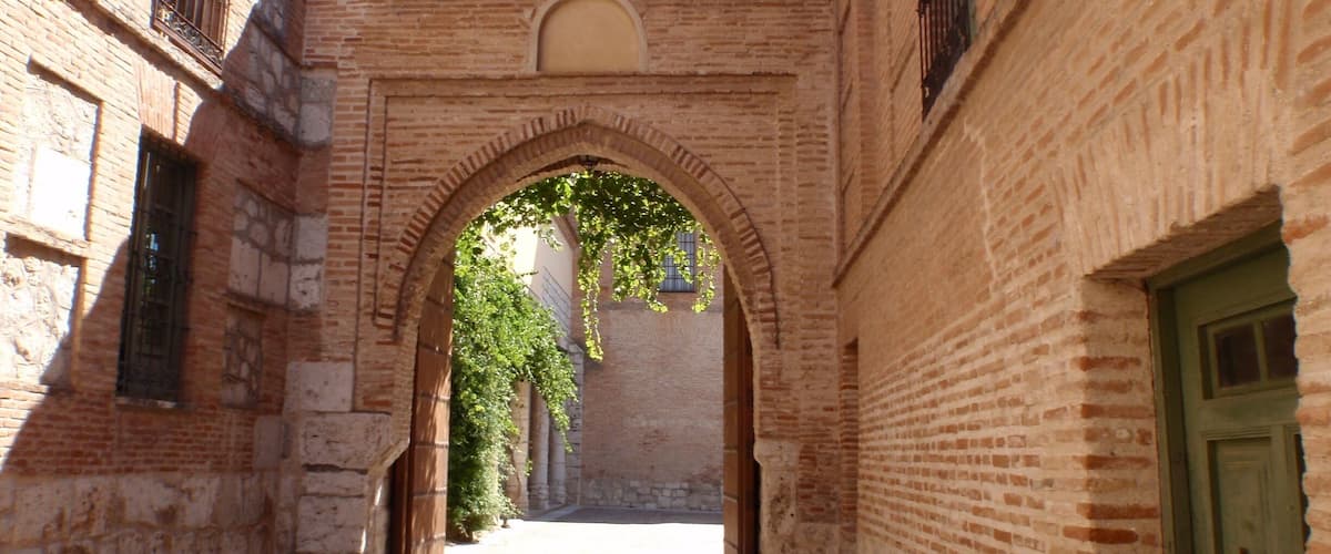 A narrow alleyway with a brick archway, tiled flooring, and a green door on the right.