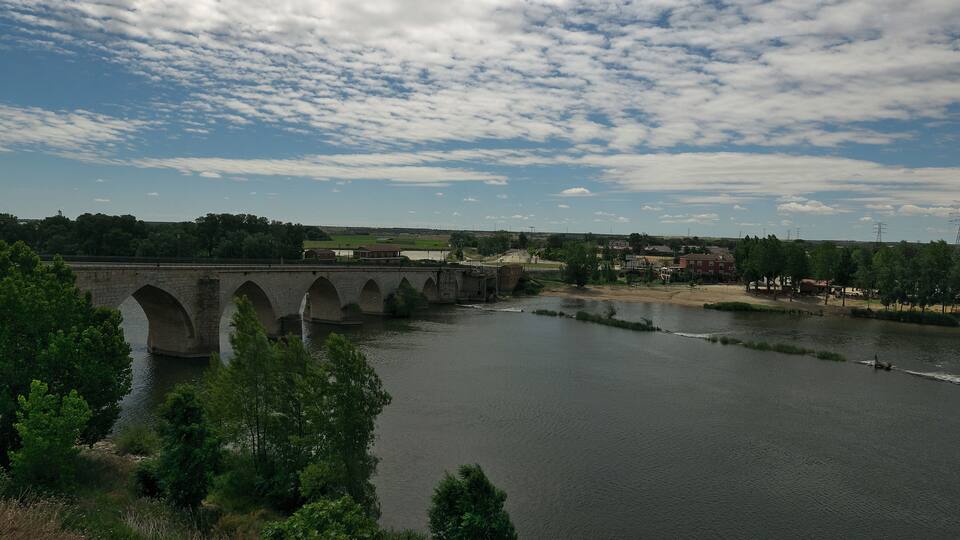 A stone bridge over a river with a town in the background.