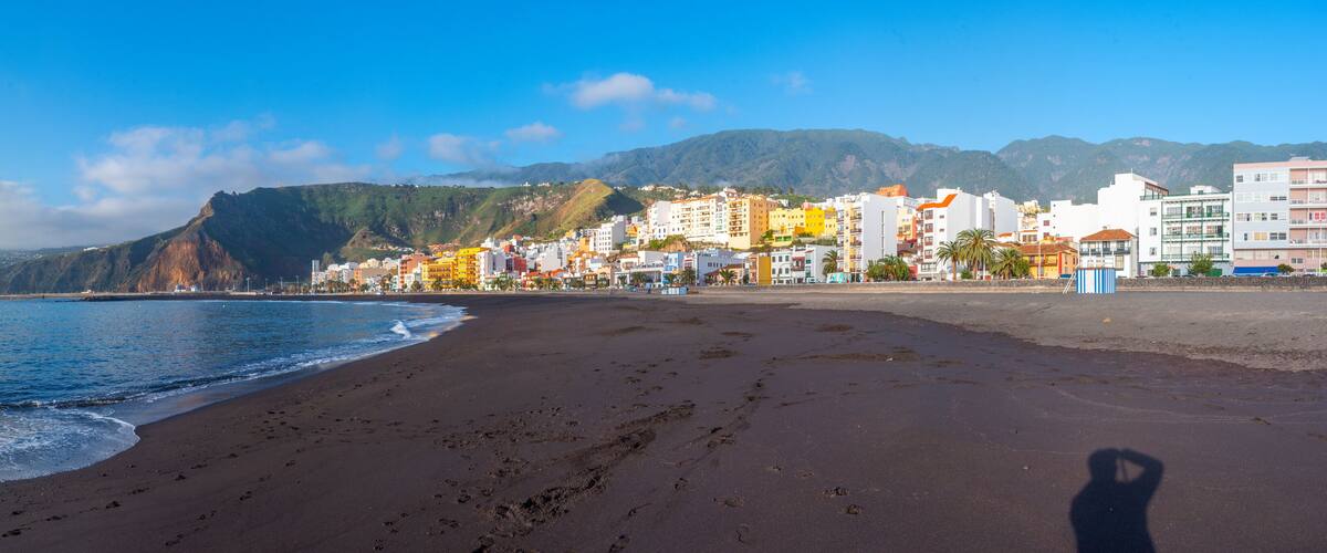 A beach with footprints, a mountain, and colorful buildings.