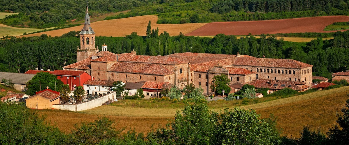 A historic church with a bell tower surrounded by rolling hills and fields.