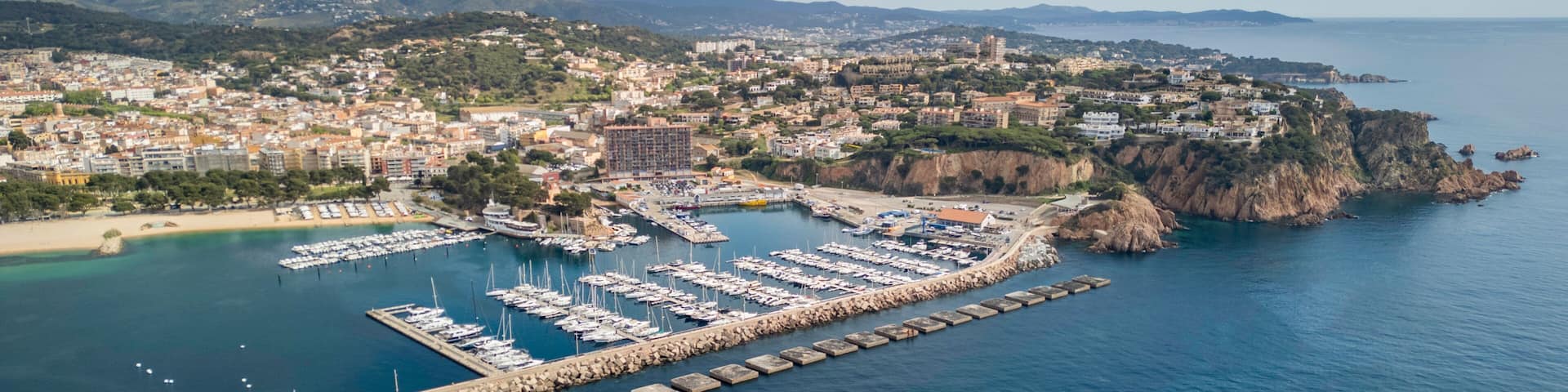 A coastal town with a marina, rocky cliffs, and a mountainous backdrop.