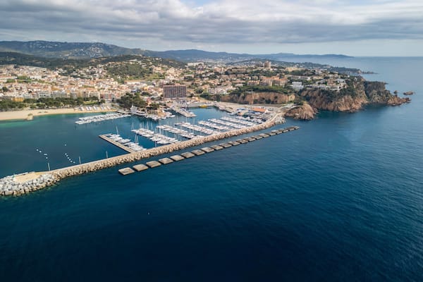 Un pueblo costero con un puerto deportivo, acantilados rocosos y montañas al fondo.