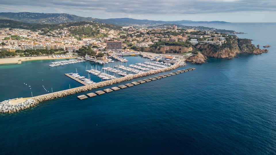 A coastal town with a marina, rocky cliffs, and a mountainous backdrop.