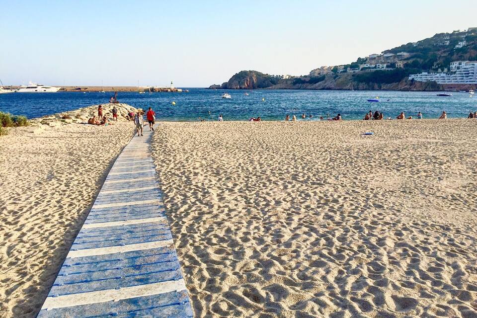 A sandy beach with a blue and white striped path leading to the water.
