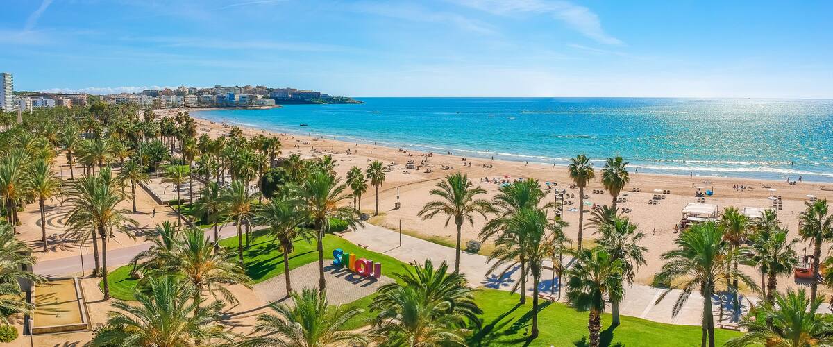 A coastal cityscape with a beach, palm trees, and a clear blue sky.