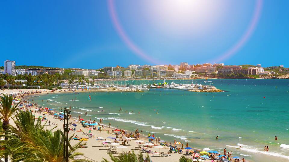 A coastal cityscape with a beach, palm trees, and a clear blue sky.