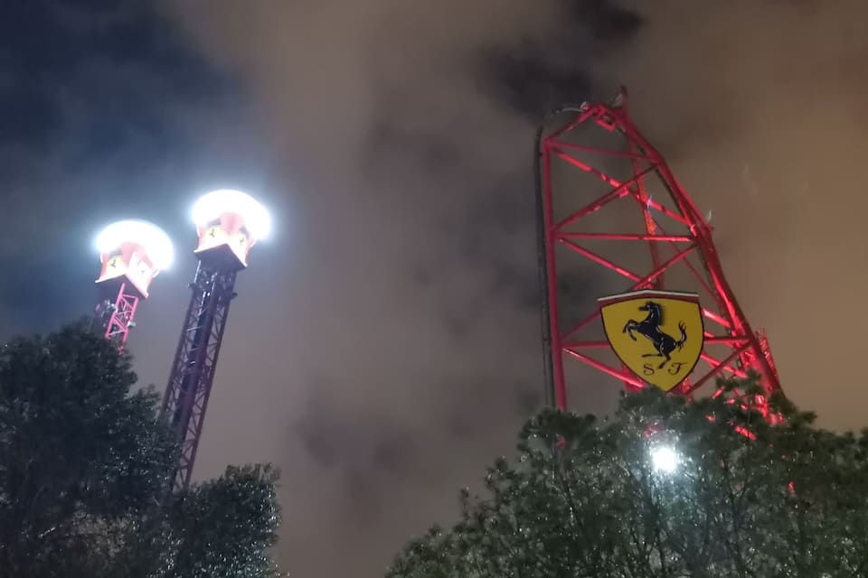 Una giostra panoramica con il logo Ferrari, luci illuminate e alberi di notte.