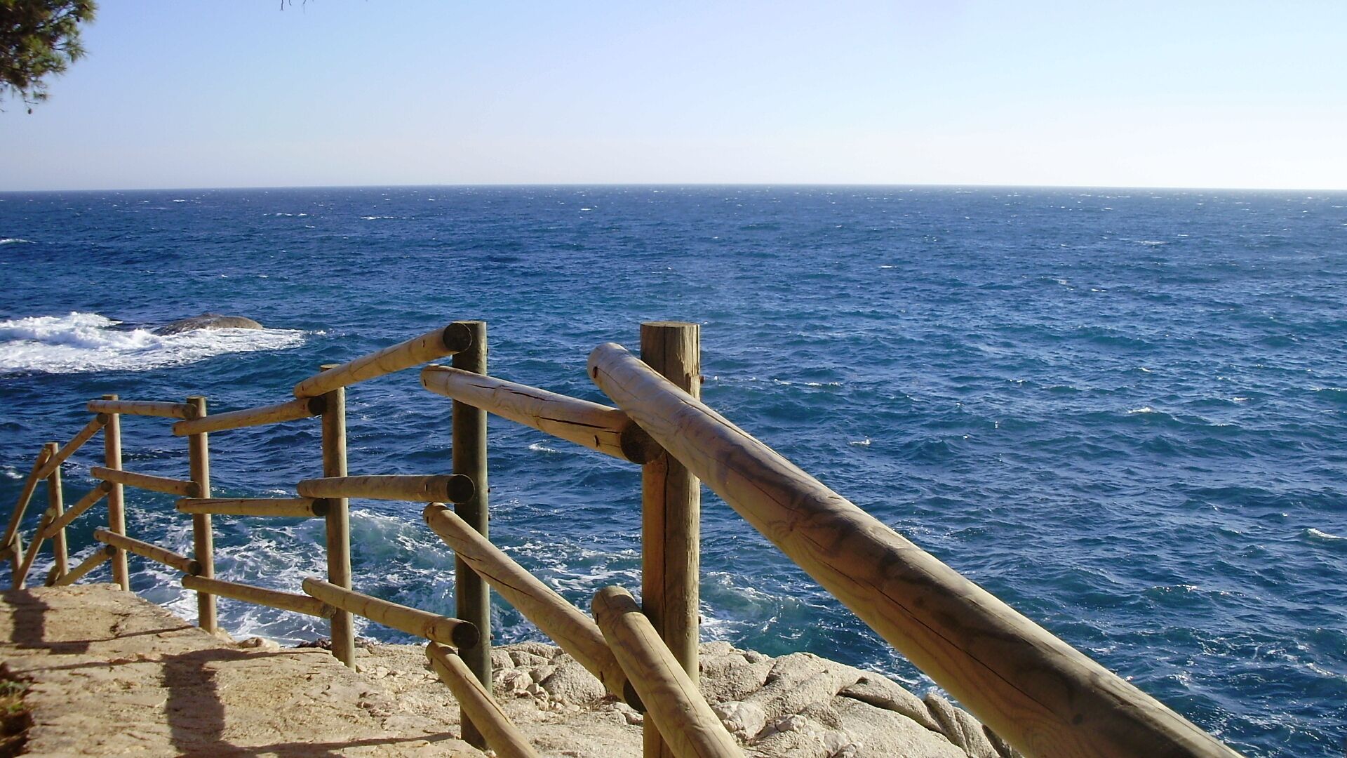 Una escalera de madera que baja hacia una costa rocosa, con el océano al fondo.