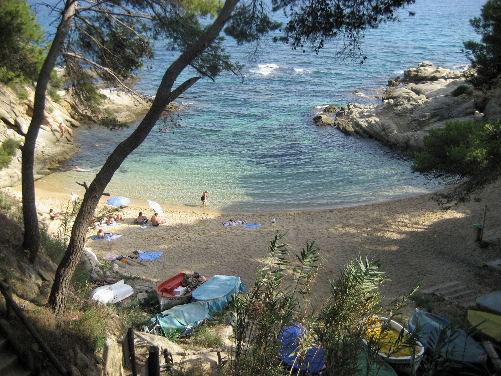 Une plage avec une eau turquoise et limpide, des affleurements rocheux et des gens qui prennent un bain de soleil.