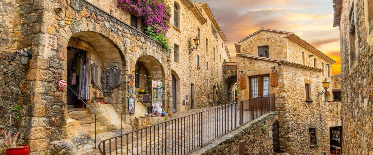 A stone-paved alleyway with arched doorways, a metal railing, and a sign reading 'Carrer de la Torre.'
