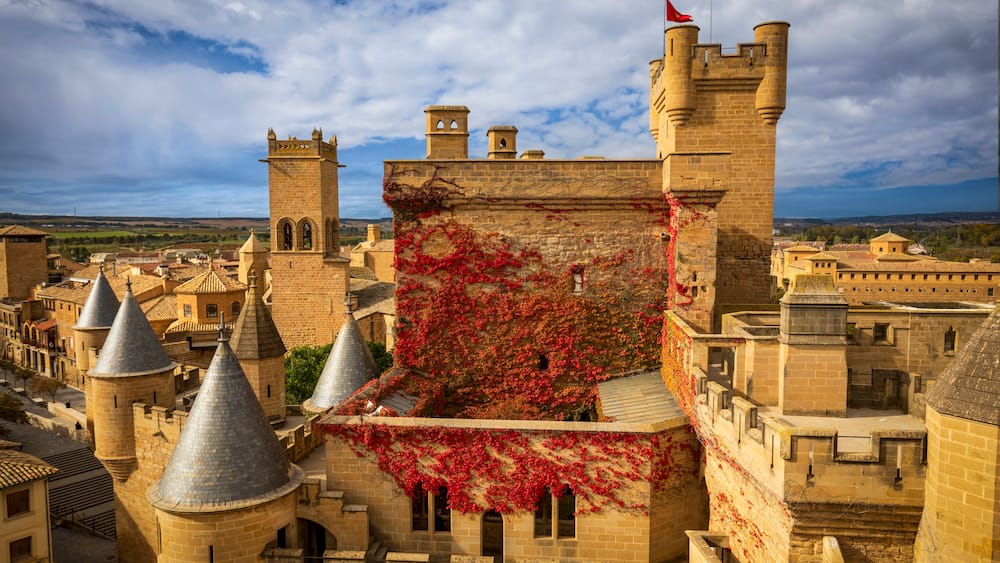 Eine historische Burg mit rotem Efeu, mehreren Türmen und blauem Himmel.