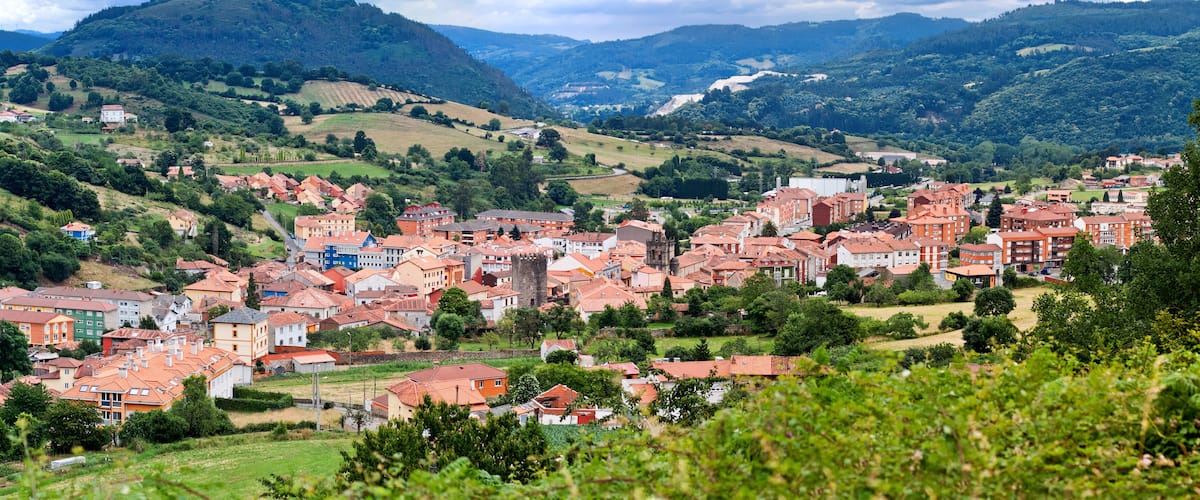 A town nestled in a valley with red-roofed buildings, surrounded by lush green hills and a prominent mountain in the background.
