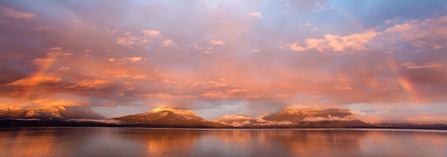 Uma cordilheira refletida em um lago calmo sob um céu de pôr do sol.