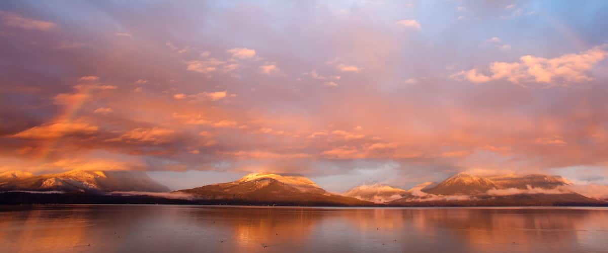 A mountain range reflected in a calm lake with a sunset sky.