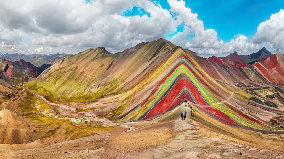 A colorful mountain range with a winding road leading up to a peak.