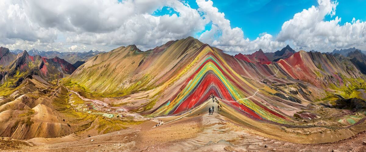 A colorful mountain range with a winding road leading up to a peak.
