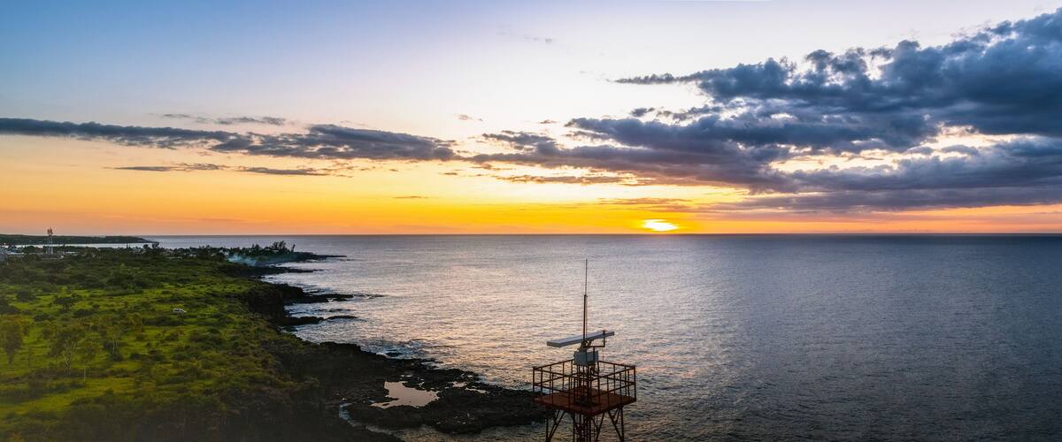 A sunset over a coastal landscape with a rocky shoreline and a communication tower.