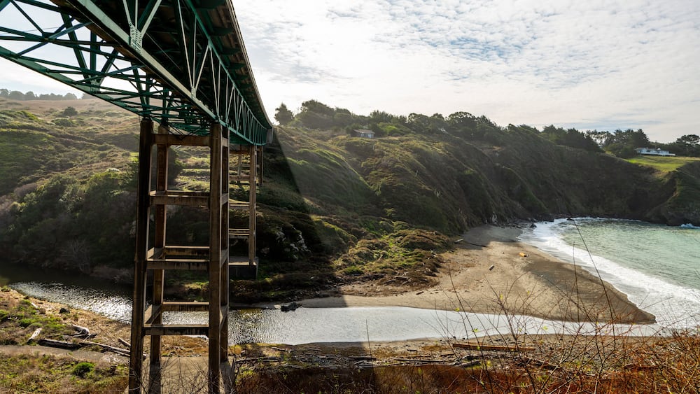 Low view of bridge above river leading to beach by cliffside houses