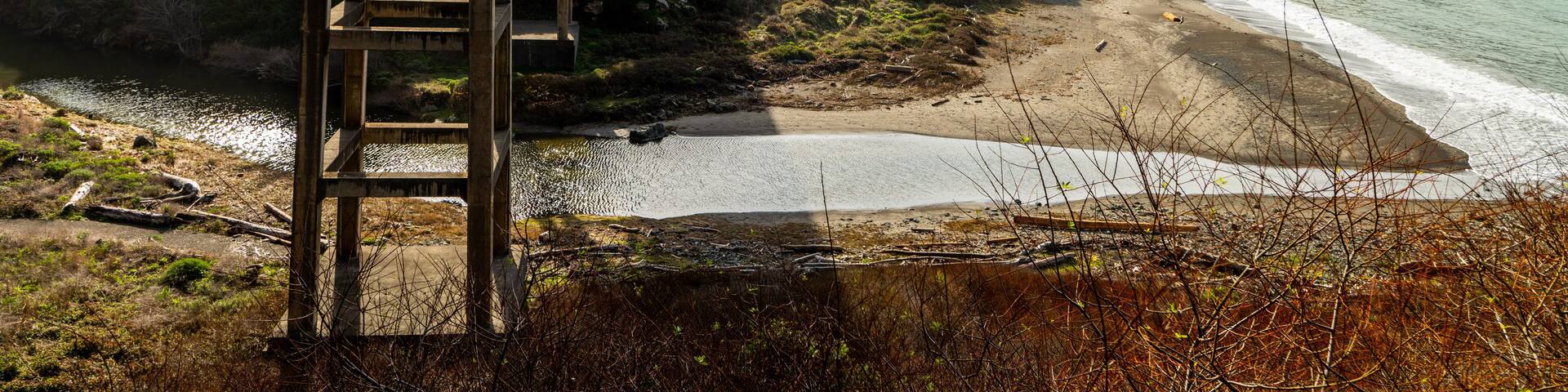 Low view of bridge above river leading to beach by cliffside houses