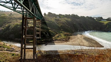 Paisagem costeira com uma ponte, praia e falésias.